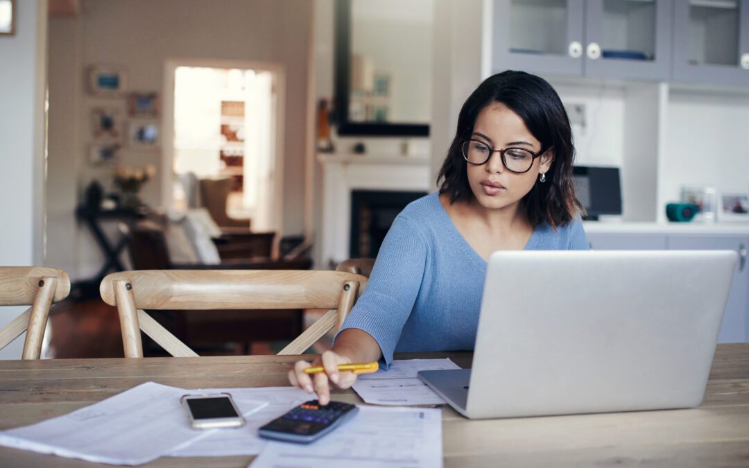 Shot of a young woman using a laptop and calculator while working from home